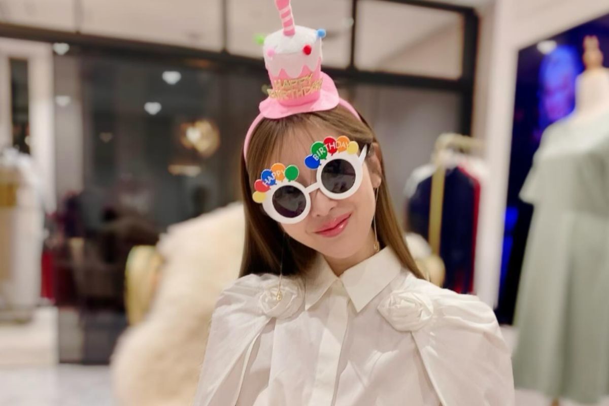 アトリエでバースデーハットとパーティーサングラスを着けておどける勝友美さん。同じサングラスをかけたぬいぐるみを抱えている